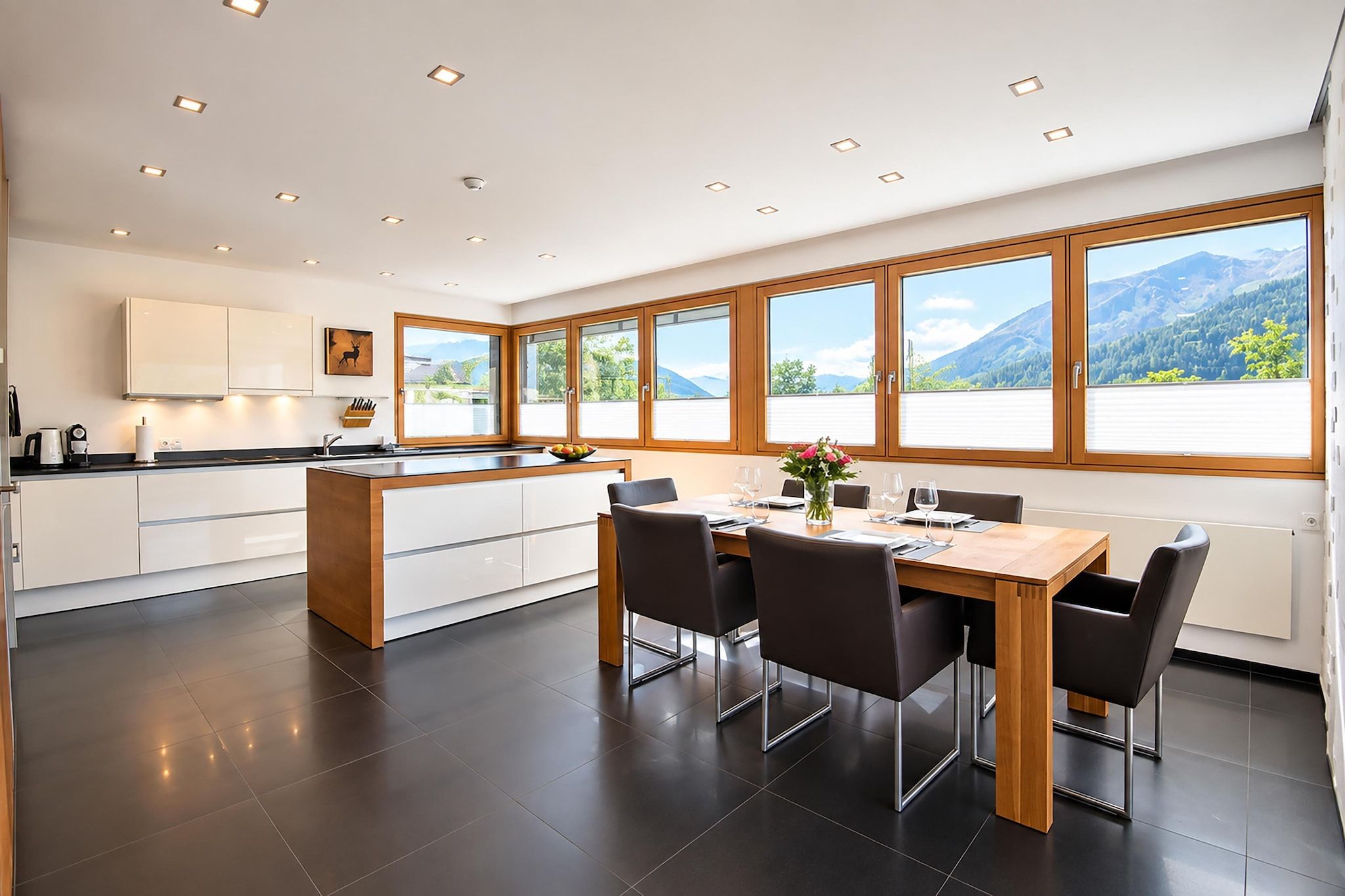 Una cocina moderna con una isla central, un comedor con mesa y sillas, y grandes ventanales con vistas a la montaña.