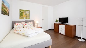 Une chambre à coucher moderne, équipée d’un lit, d’une télévision, d’un bureau et d’une lampe sur pied.