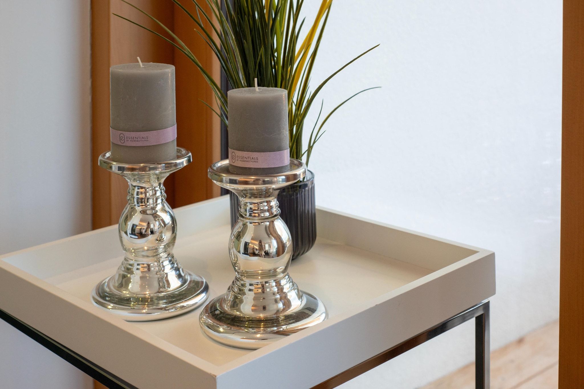 Two candles on a tray with a potted plant in the background.