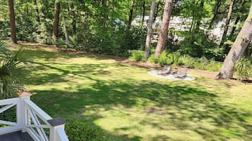 A deck with a railing, a grassy area, and a small fire pit surrounded by trees.