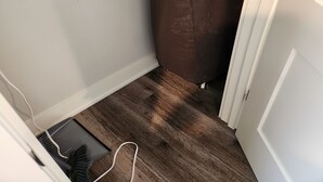Een hoek van een kamer met een bruin bedekt voorwerp, een witte deur en een houten vloer.