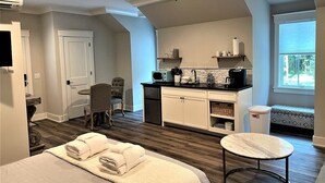 Een hotelkamer met een bed, een tafeltje, een kitchenette, een stoel, een plafondventilator en een raam.