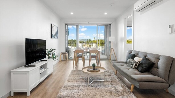 A modern living room with a flat-screen TV, a sofa, a coffee table, and a balcony with a dining set. - Stylish 2BR + Sofa Bed Apartment | Prospect (Prospect)