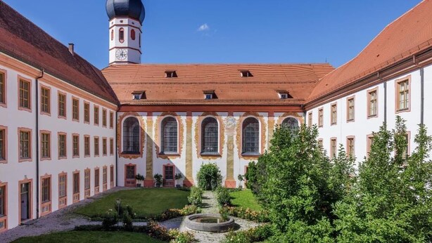 A courtyard with a central building featuring arched windows and a tower with a dome. - Kloster Beuerberg  (Beuerberg)