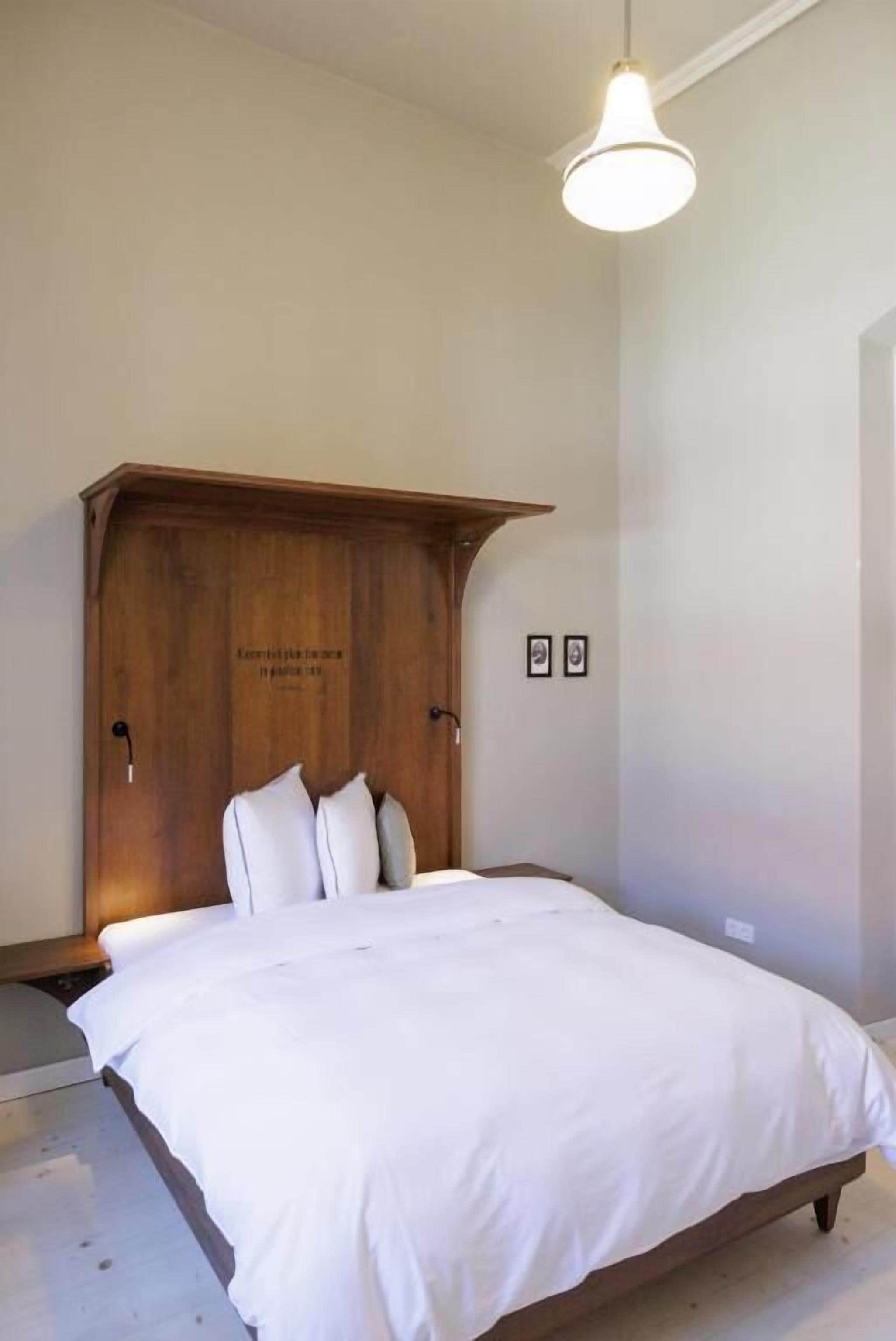 A bedroom with a wooden headboard, a white bedspread, and a hanging light fixture.