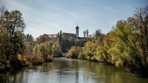 A river with trees and a building with a tower in the background. - Kloster Beuerberg  (Beuerberg)
