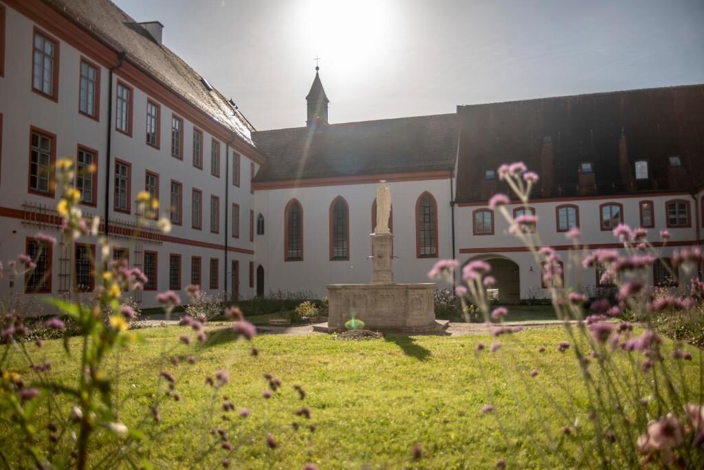 A courtyard with a fountain, surrounded by buildings with arched windows and a tower.