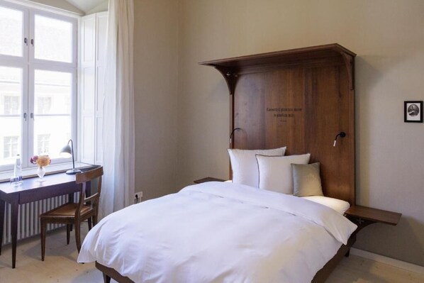 Une chambre à coucher avec un grand lit, une tête de lit en bois, un bureau avec une chaise et une fenêtre avec des rideaux.