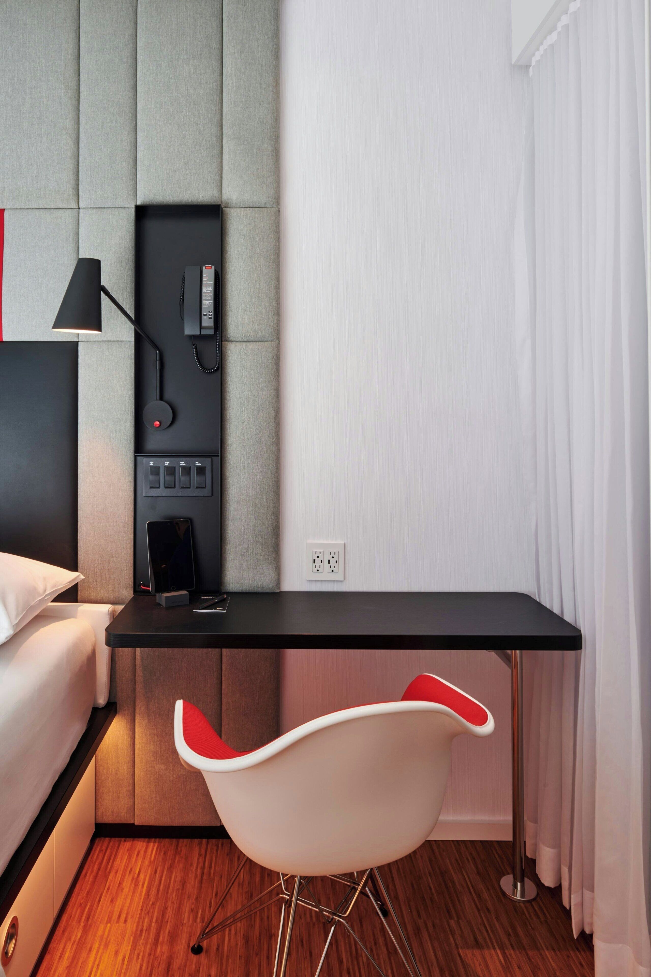 Ein modernes Hotelzimmer mit einem Bett, einem Schreibtisch mit Telefon, einem Sessel und einer Wandbedienung.