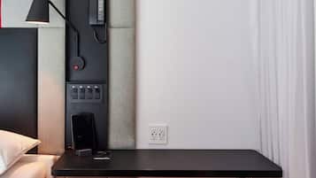 Ein modernes Hotelzimmer mit einem Bett, einem Schreibtisch mit Telefon, einem Sessel und einer Wandbedienung.