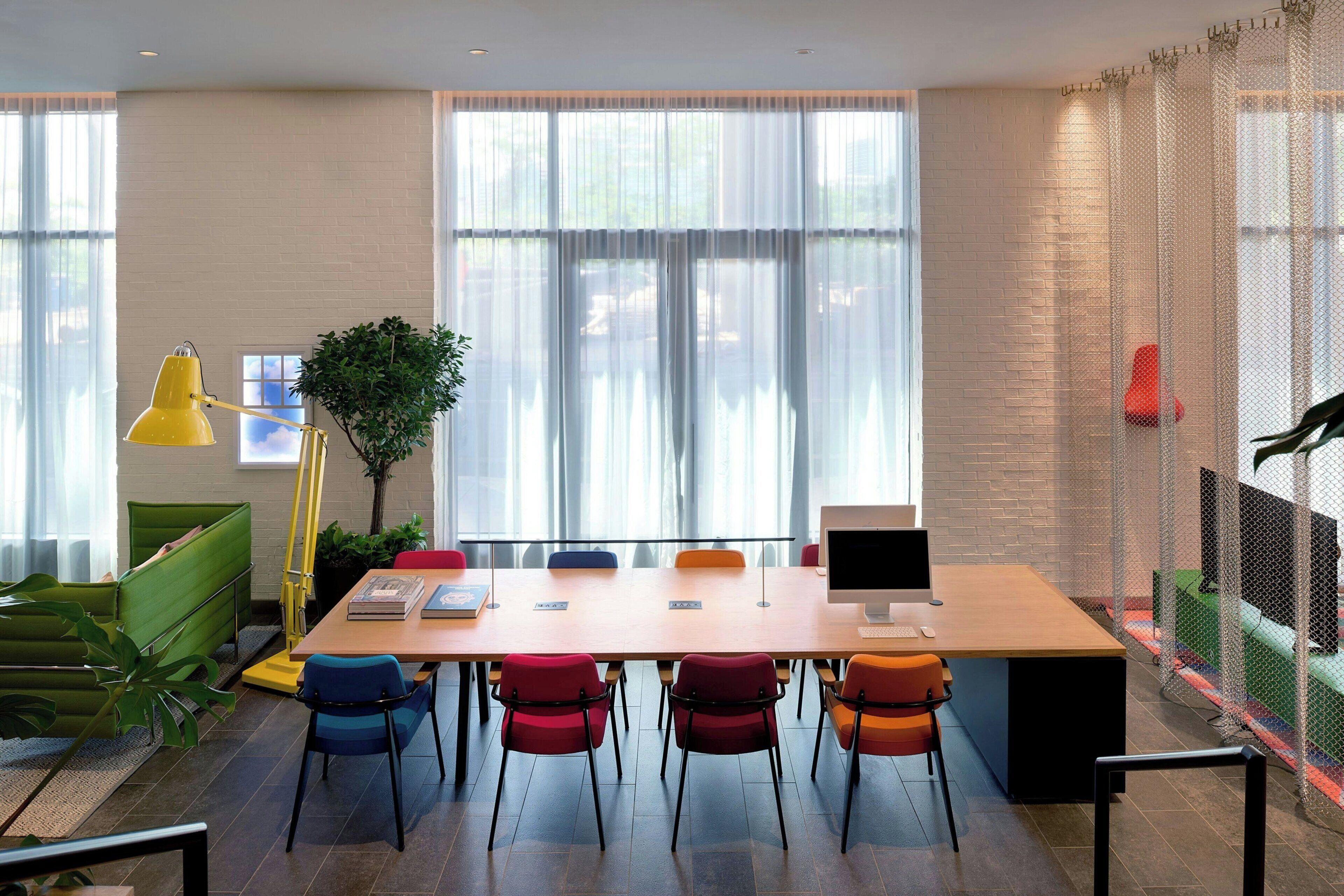 Un espacio de oficina moderno con una mesa larga, varias sillas, un escritorio con una computadora y una planta.