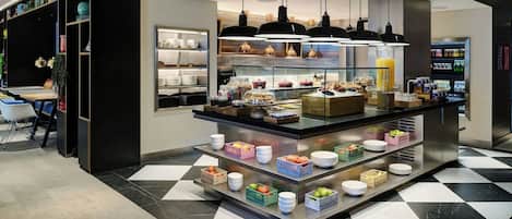 A modern breakfast bar with a variety of food items and beverages, surrounded by shelves with books and decorative items.