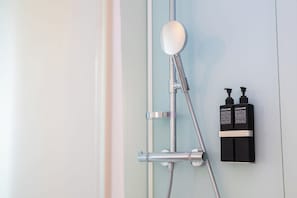 Een douche met een handdouche en twee shampoo flessen.