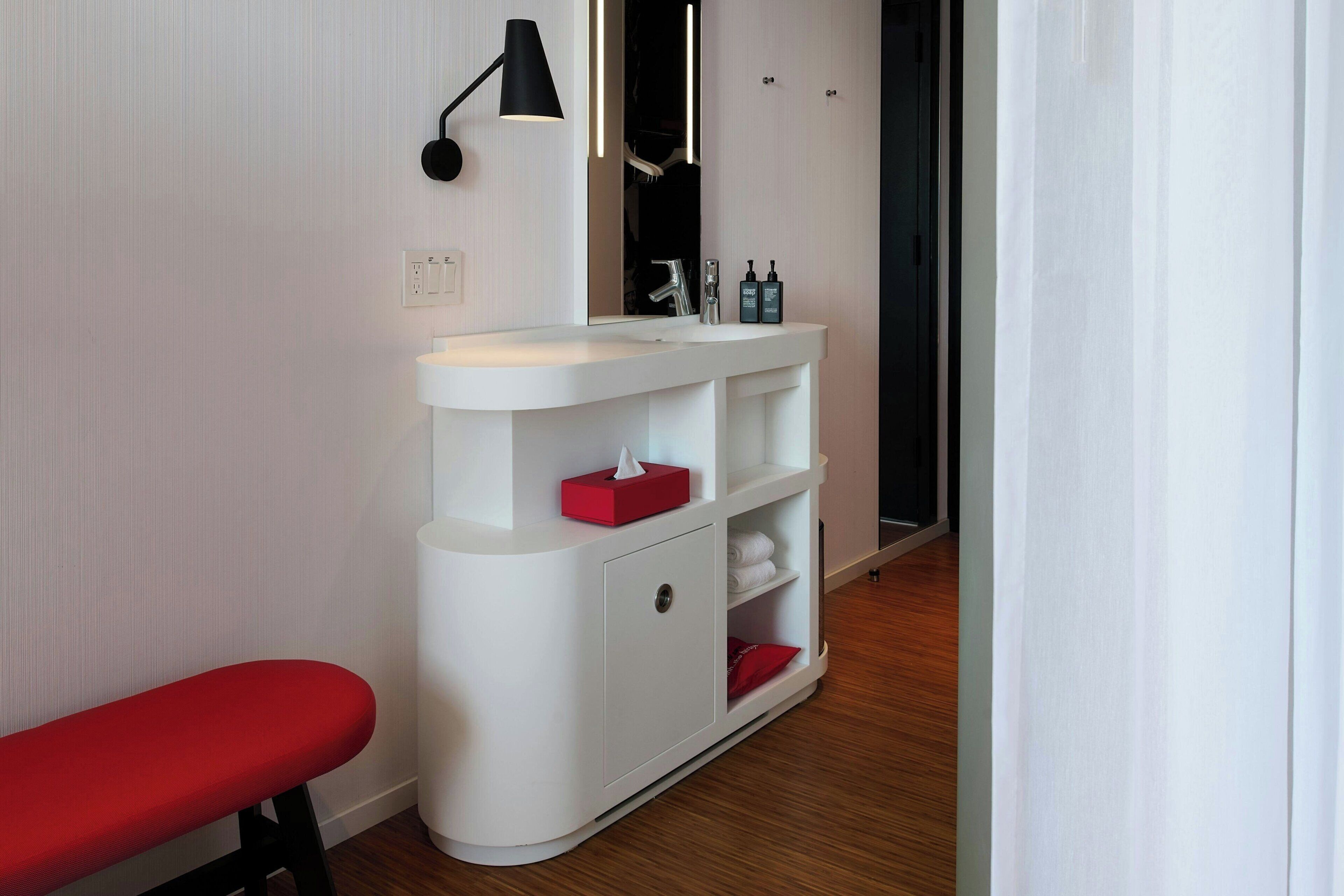 A modern bathroom with a white vanity, a red bench, and a mirror above the sink.