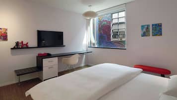 A modern bedroom with a bed, a desk, a chair, a television, and artwork on the walls.