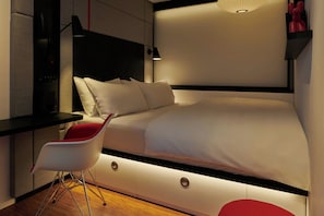 Een moderne slaapkamer met een bed, nachtkastje, stoel en een wandlamp.