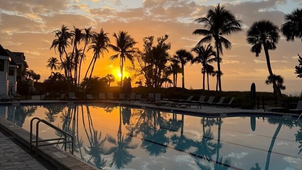 A swimming pool with palm trees and a sunset in the background. - Beachfront 2BR Condo at Casa Ybel Resort: Top Floor, Private Balcony Ocean Views (Sanibel)