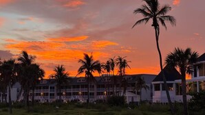 A beachfront hotel with multiple-story buildings, palm trees, and a sunset sky. - Beachfront 2BR Condo at Casa Ybel Resort: Top Floor, Private Balcony Ocean Views (Sanibel)