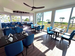 Ein Restaurant mit blauen Stühlen und Tischen, großen Fenstern und einem Deckenventilator.