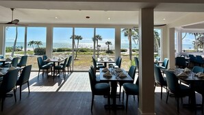 A restaurant with tables and chairs, large windows, and a view of the beach. - Beachfront 2BR Condo at Casa Ybel Resort: Top Floor, Private Balcony Ocean Views (Sanibel)