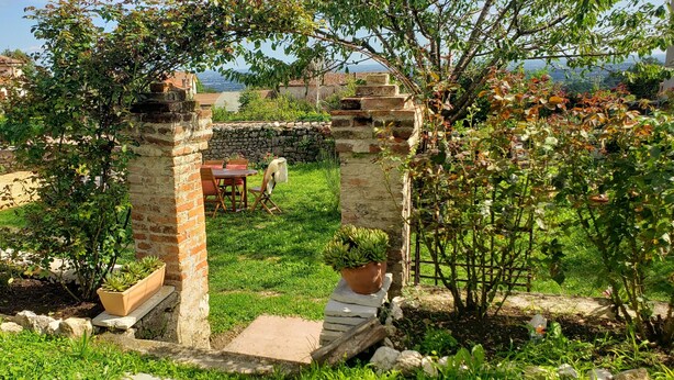 Un jardin agrémenté d’une arche en pierre, d’une table en bois et de plantes en pot.