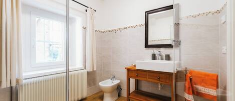 Une salle de bain équipée d’un bidet, d’un lavabo, d’un miroir et d’une fenêtre avec des rideaux.