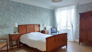Een slaapkamer met een houten bed, twee nachtkastjes, een stoel, een radiator en een kledingkast.