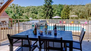 Uma área de refeições ao ar livre com vista para a piscina, deck de madeira e guarda-corpo de metal.