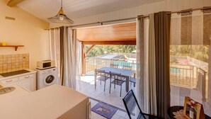 Quarto com cozinha, máquina de lavar, mesa e vista para uma piscina e área externa.