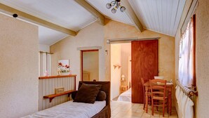 Quarto com cama, uma cadeira de madeira, uma mesinha, uma porta e um radiador.
