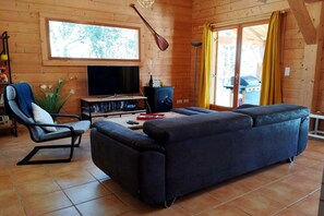 Ein Holzblockhaus-Interieur mit einer Couch, einem Sessel, einem Fernseher, einem Kamin und einem Fenster mit Vorhängen.