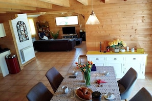 Ein gemütliches Zimmer mit Esstisch für zwei Personen, einer Couch und einem Fernseher im Hintergrund.