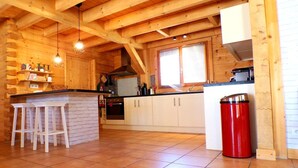 A wooden cabin interior with a kitchen area, wooden beams, a tiled floor, and a red trash can. - Home with Enclosed Garden near Sarlat (PECHS DE L'ESPERANCE)