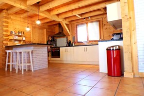 Ein Holzblockhaus-Interieur mit Küchenbereich, Holzbalken, gefliestem Boden und einer roten Mülltonne.