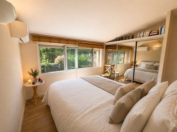 Une chambre avec un grand lit, une petite table avec des bougies, une chaise et une fenêtre donnant sur un paysage verdoyant.