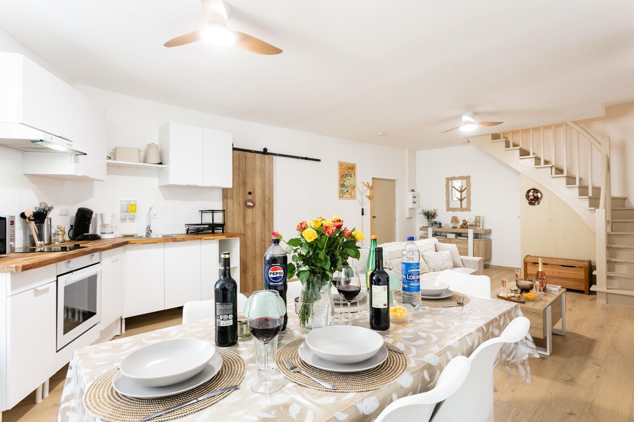 Una cocina moderna con armarios blancos, encimera de madera y comedor con mesa para dos.