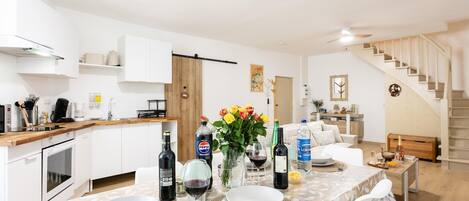 Una cocina moderna con armarios blancos, encimera de madera y comedor con mesa para dos.