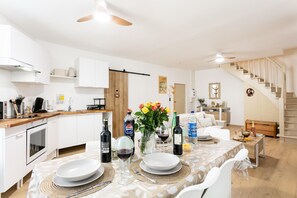 Una cocina moderna con armarios blancos, encimera de madera y comedor con mesa para dos.