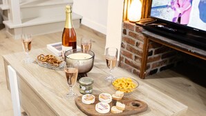 A wooden table with snacks, cheese, and drinks, a candle, and a bottle of champagne in a room with a TV and fireplace. - Apartment in Martel City Center (MARTEL)