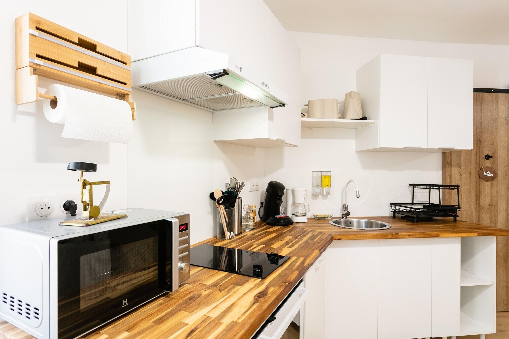 Een moderne keuken met een ingebouwde magnetron, een houten aanrecht, witte kastjes, een koffiezetapparaat en een spoelbak.