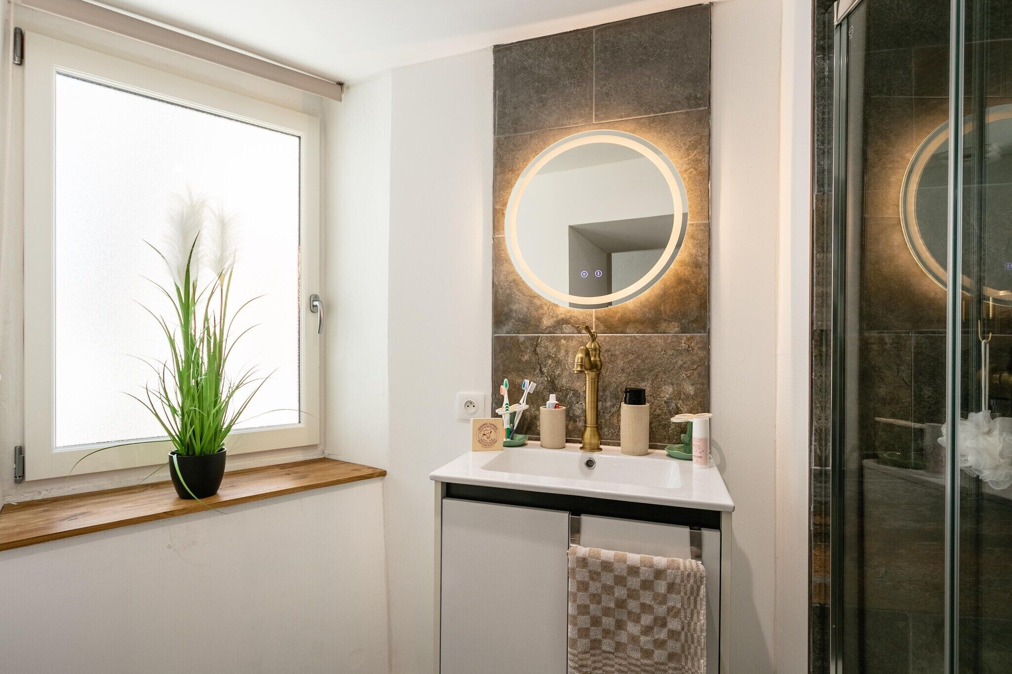 Een badkamer met een raam, een spiegel, een wastafel en een douche.
