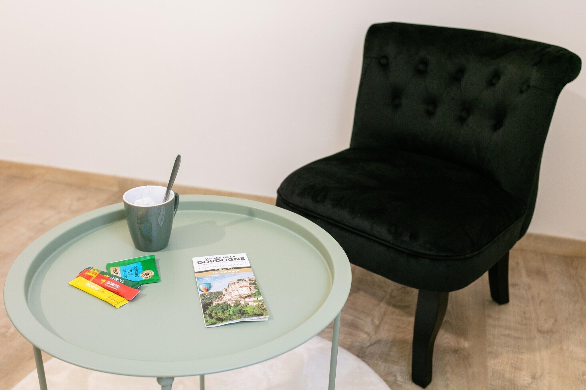Une table ronde en verre, accompagnée d’une chaise noire, d’une tasse et de quelques brochures de voyage.
