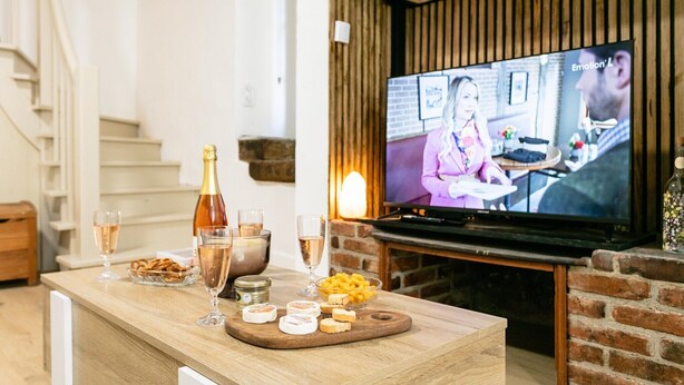 A living room with a wooden bar area, a television displaying a show, and a brick fireplace. - Apartment in Martel City Center (MARTEL)