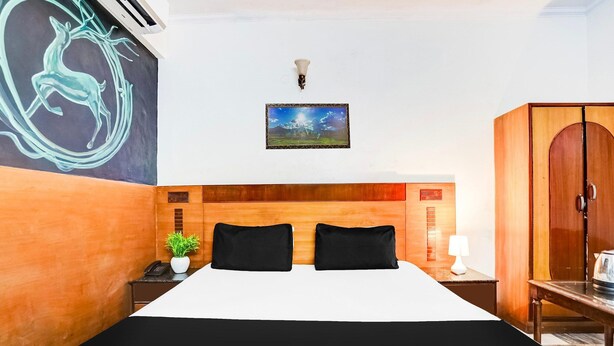 Une chambre d’hôtel comprenant un lit, une table de chevet, une lampe, une armoire, un tableau accroché au mur et un appareil de climatisation fixé au mur.