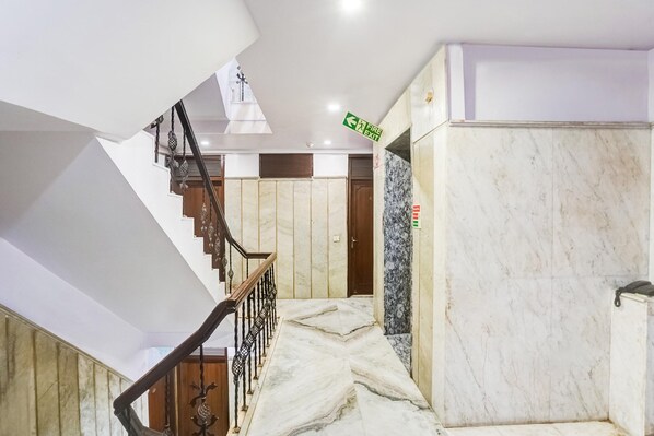 A staircase with a wooden handrail, a marble wall, and a door with a fire exit sign.