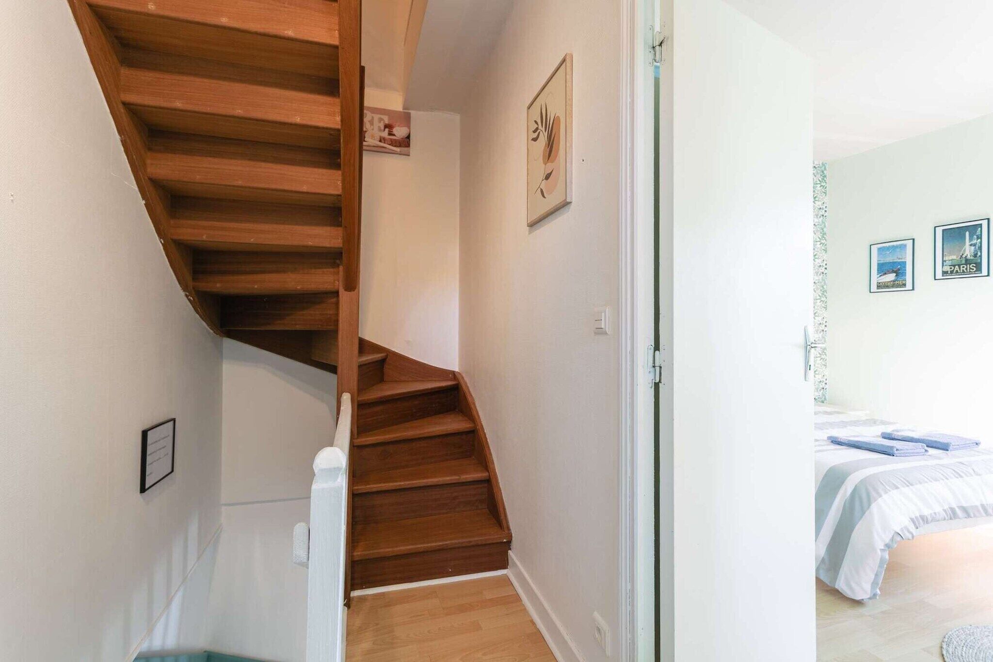 Een trap met houten treden die leidt naar een slaapkamer met een bed en twee foto's in lijsten aan de muur.