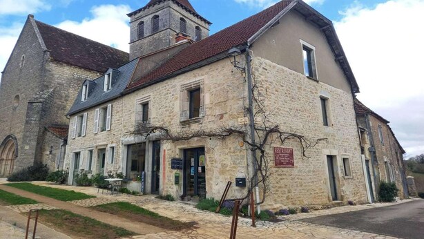 A stone building with a bell tower, a restaurant sign, and a paved walkway. - Bastide Village Retreat in Montfaucon (MONTFAUCON)