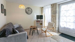 A living room with a sofa, a chair, a small table, a TV, and a clock on the wall. - Bastide Village Retreat in Montfaucon (MONTFAUCON)