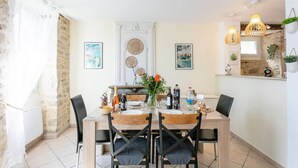 A dining area with a wooden table, black chairs, and a vase with flowers. There are wall-mounted lights and a stone wall. - Bastide Village Retreat in Montfaucon (MONTFAUCON)