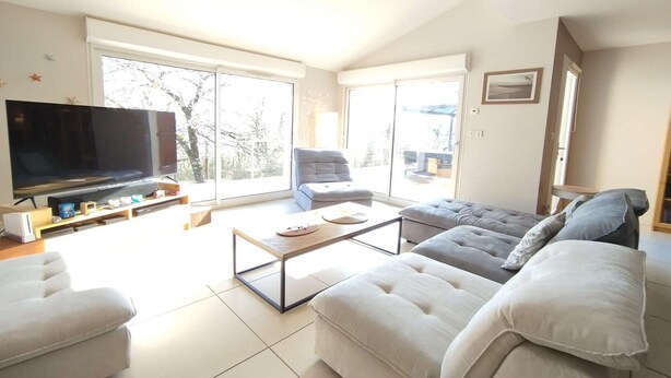 A modern living room with a flat-screen TV, two sofas, a coffee table, and large windows. - Charming 4-Bedroom House in the Heart of the Lot (LACHAPELLE AUZAC)